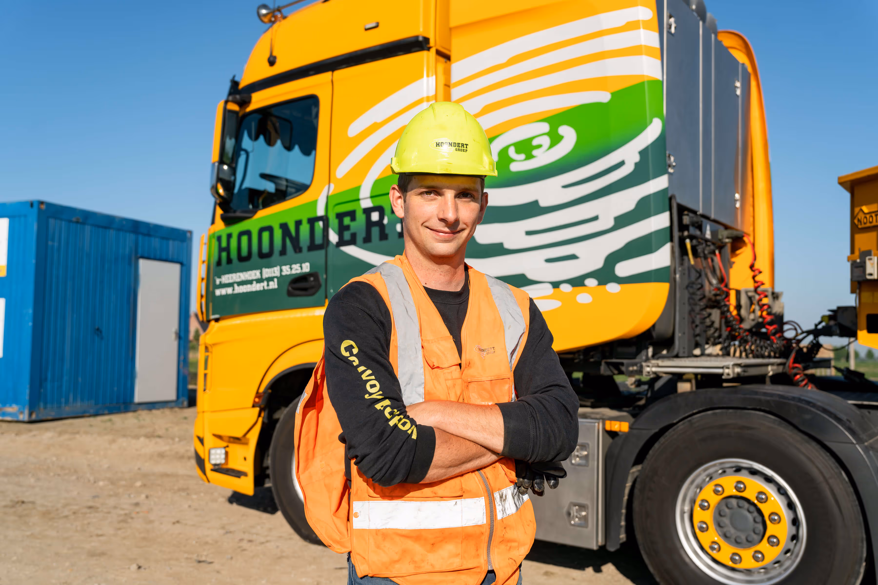 Bouwvakker met veiligheidshelm en veiligheidsvest voor een vrachtwagen op een bouwterrein.